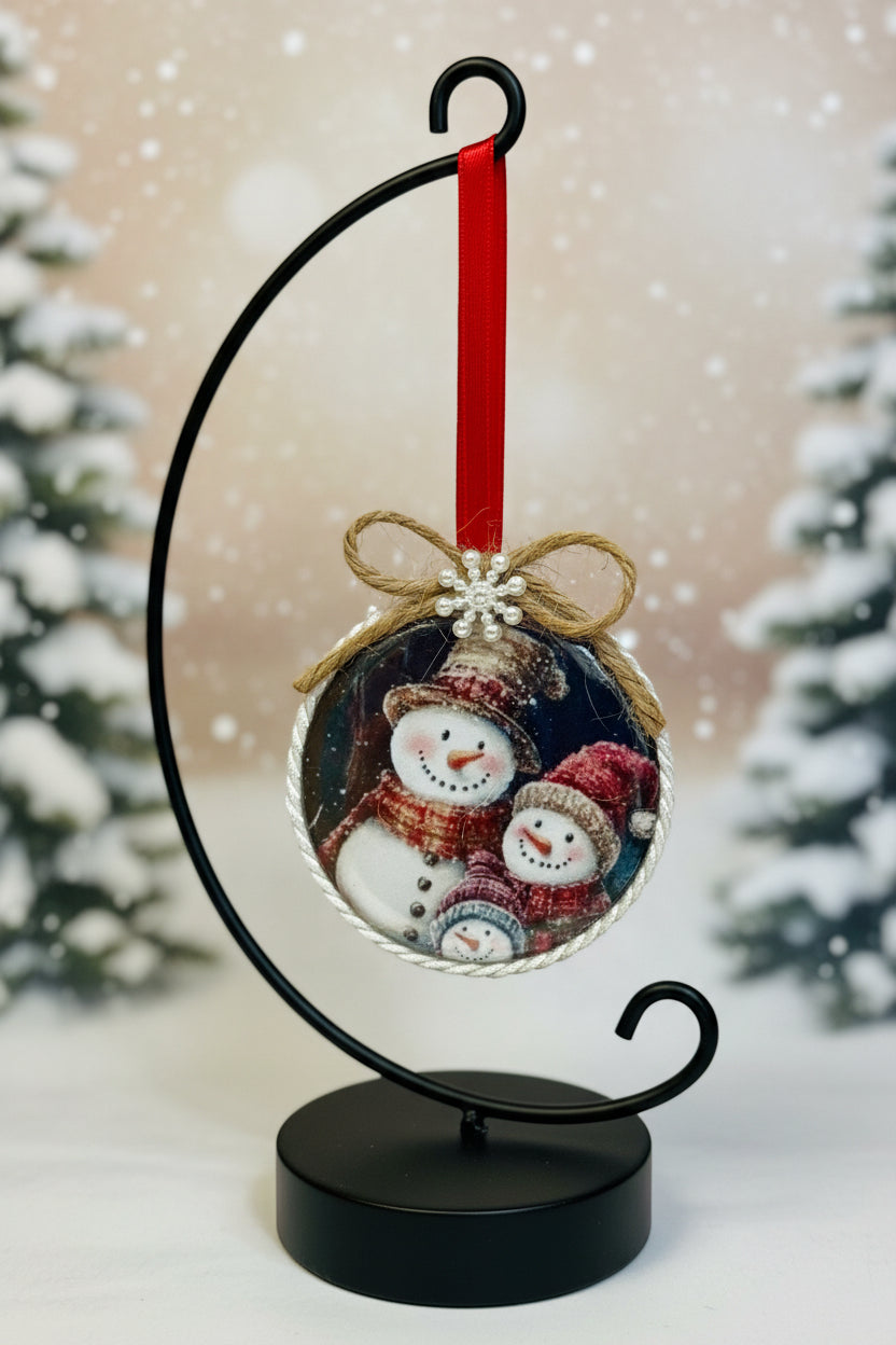 Decorative Christmas ornament with a family of snowmen and a red ribbon on a white background