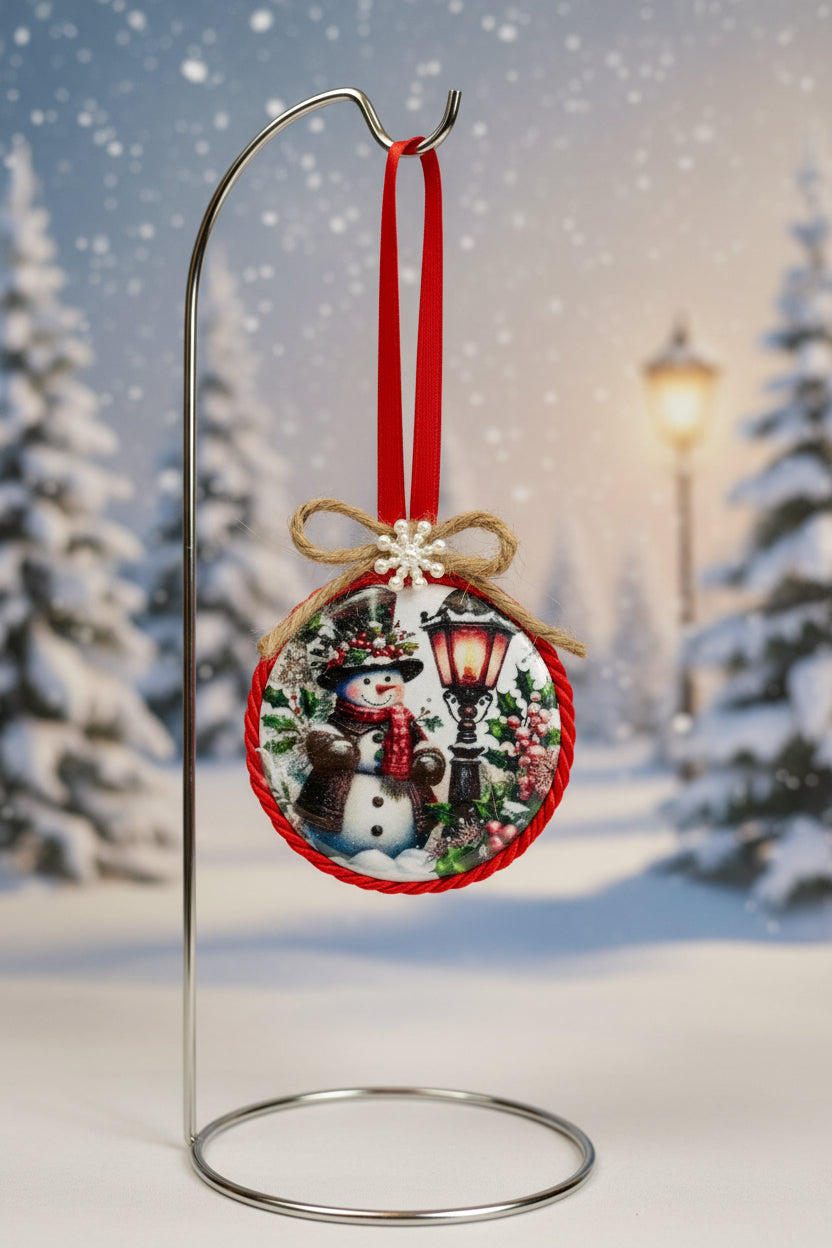 Decorative Christmas ornament with a snowman standing near a holiday lantern design on a plain background